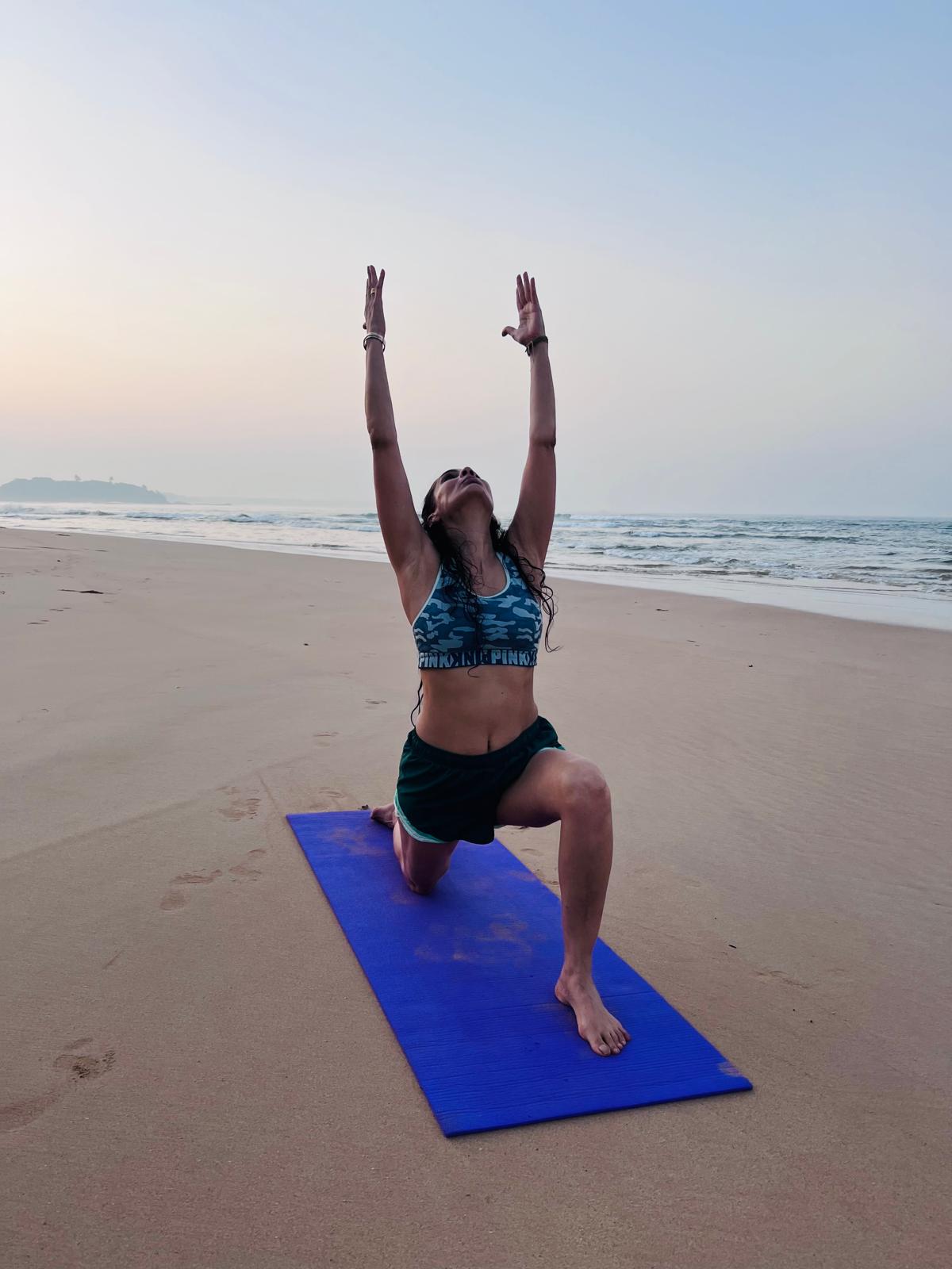 Woman practicing a low lunge yoga pose on a blue mat on a Rhode Island beach at sunrise