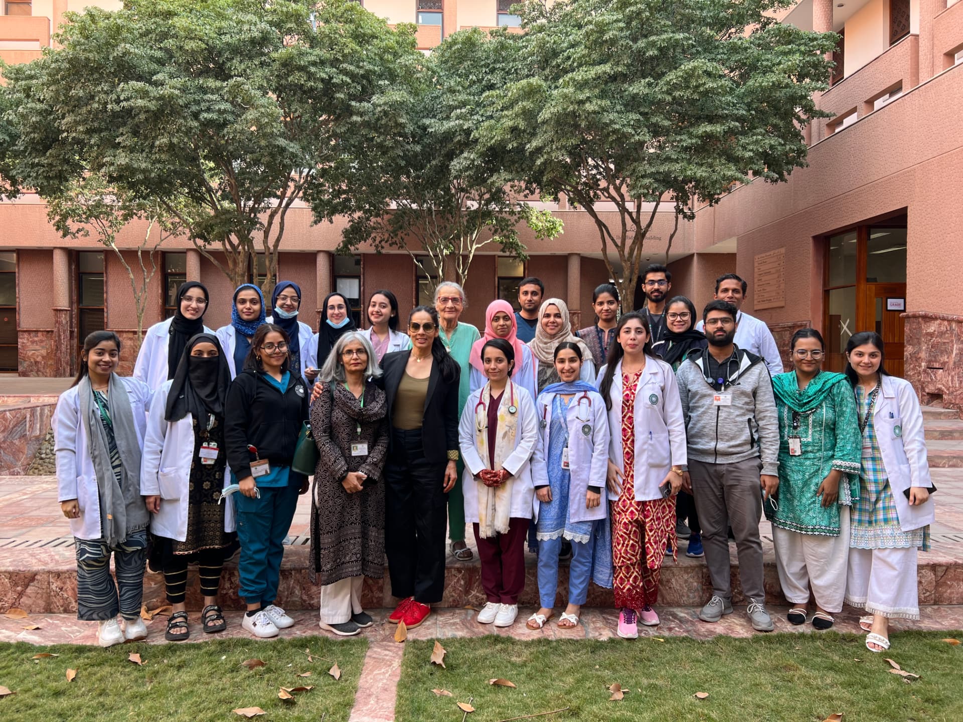 A large group of medical professionals and students in white lab coats posing together in an outdoor courtyard.