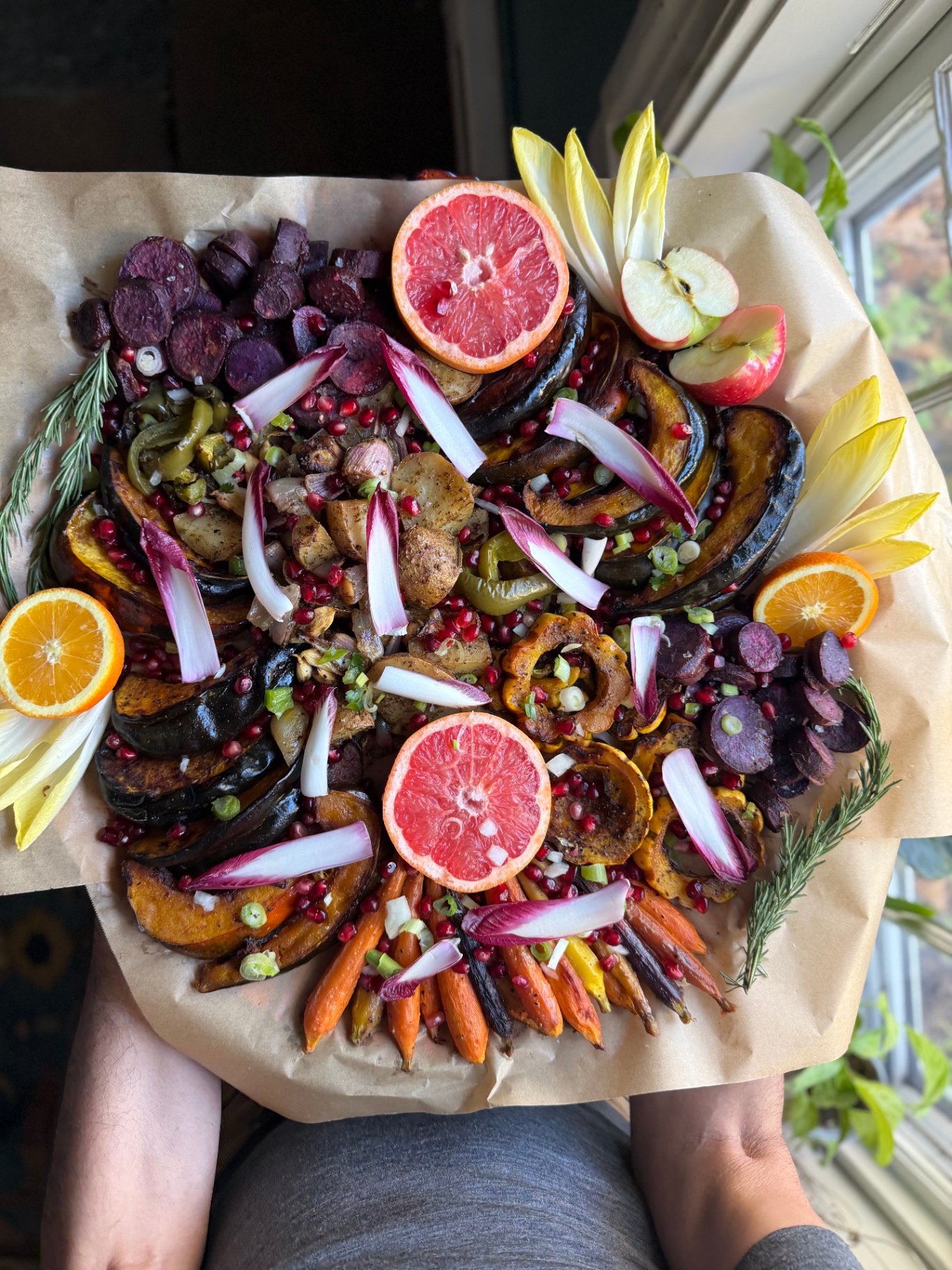 An overhead platter of roasted squash, carrots, citrus, endive, apples and pomegranate seeds arranged on parchment paper.